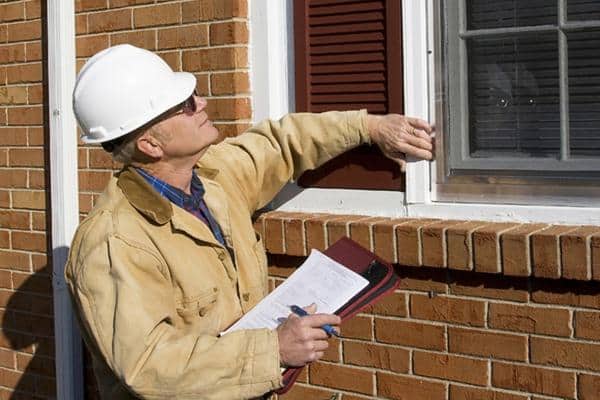 Home Inspections professional wearing a hard hat and carrying a clipboard while meticulously inspecting the exterior window of a brick home.