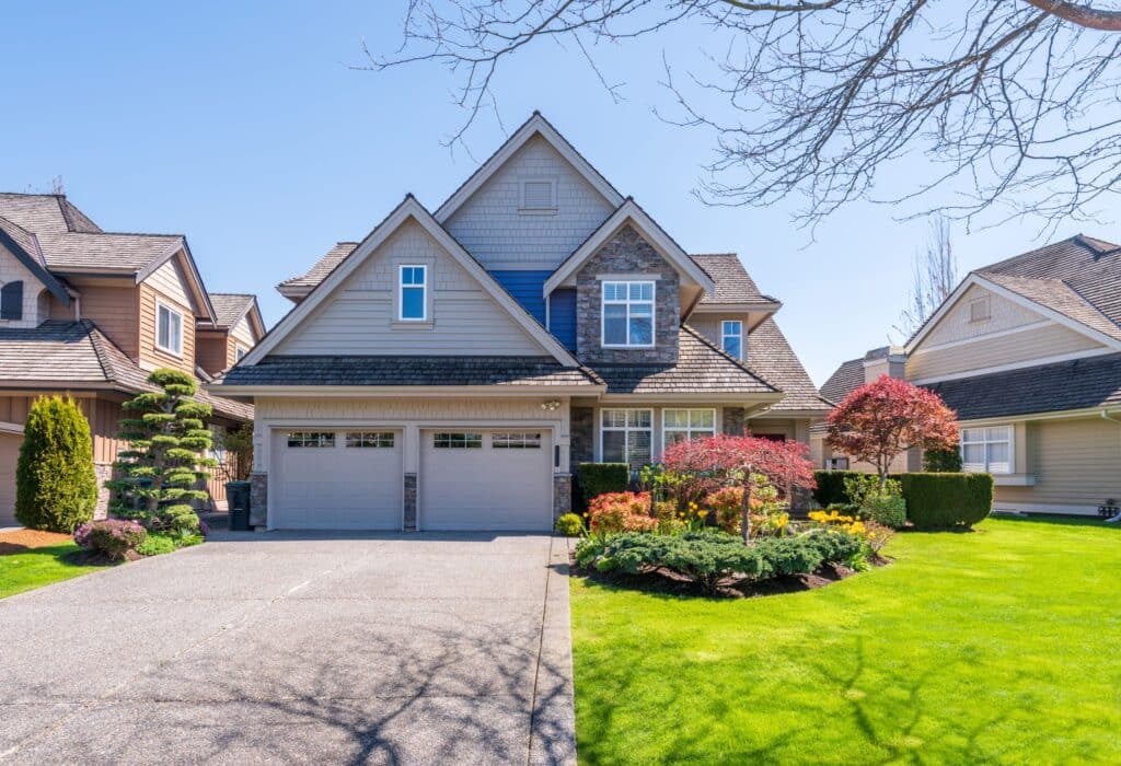 A luxury house with a multi-gabled roof and stone accents features a two-car garage and vibrant landscaping under a clear blue sky.